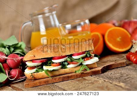 Large Baguette Sandwich Cut In Half Filled With Hard-boiled Egg, Arugula Salad, Tomatoes And Radish 