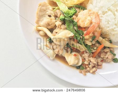 Spicy Fried Basil Leaf And Vegtable With Seafood And Fried Egg With Rice In White Plate On White Bac