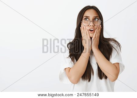 Indoor Shot Of Impressed Stunned Emotive Woman With Dark Hair In Glasses, Holding Palms On Cheeks, G