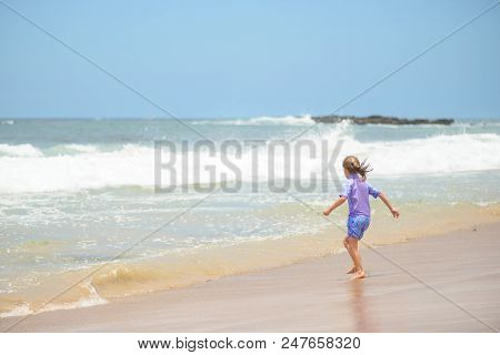 Happy Girl In Purple Swimsuit Running On The Beach In The Waves, Family On Vacation, View From Behin