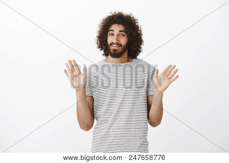 Careless Handsome Male Model With Afro Hairstyle And Sick Beard, Raising Palms In Surrender And Smil