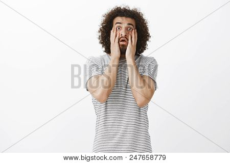 Portrait Of Shocked Fed Up Finny Eastern Guy With Beard And Afro Haircut, Holding Hands On Cheeks An