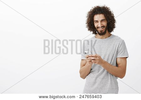 Happy Carefree Good-looking Guy With Beard And Afro Haircut, Holding Smartphone And Laughing With Pl