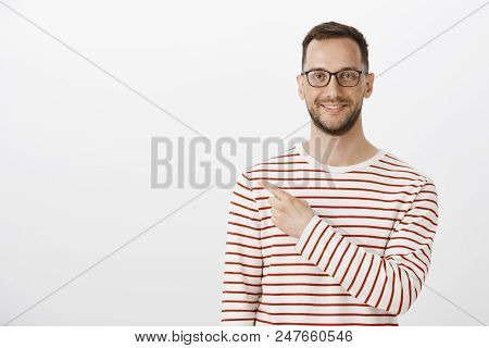 Portrait Of Satisfied Happy Aduly Man With Bristle In Trendy Glasses And Striped Pullover, Pointing 