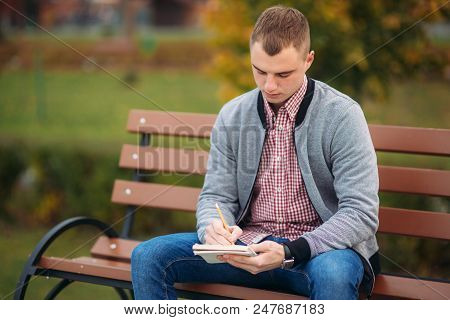 A Cute Student Writes Down His Thoughts In His Notebool Using A Pensil.