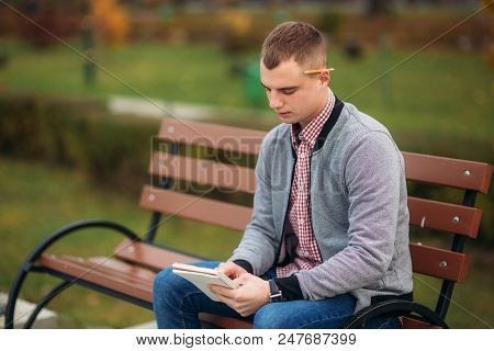 A Cute Student Writes Down His Thoughts In His Notebool Using A Pensil.