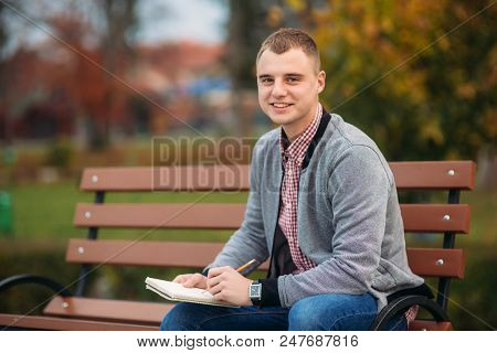 A Cute Student Writes Down His Thoughts In His Notebool Using A Pensil.