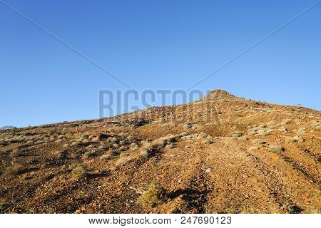 Stony Pinnacle With Scrubby Vegetation Under Blue Sky In Namibia.