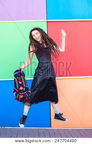Cheerful Beautiful Slim Girl With Dreadlocks, Rastaman, In A Black Dress And Sneakers, Jumps Against