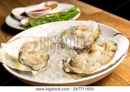 Close Up Of Fresh Opened Oyster Offered As Top View On Crushed Ice In White Dish On Wood Table.