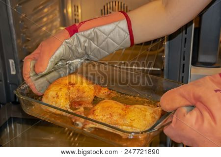 Female Hands In Heat-insulated Gloves Holding A Glass Bowl With Baked Tender Chicken Thighs