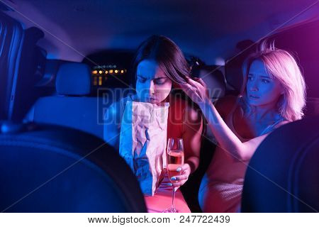 Brunette Girl Is Sick. She Is Vomiting. Young Woman Has A Paper Bag In Her Hands. She Is Looking Dow