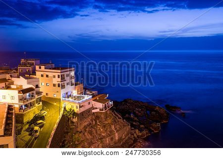 Buildings On The Rocks And Atlantic Ocean Night Scene. Puerto De Santiago. Tenerife Islans, Canarias