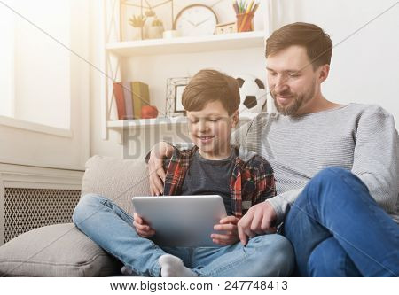 Father And Son Spending Time Together And Using Digital Tablet On Sofa At Home