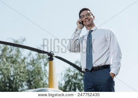 Mood-boosting Chat. Pleasant Young Businessman Chatting On The Phone And Smiling Brightly While Stan