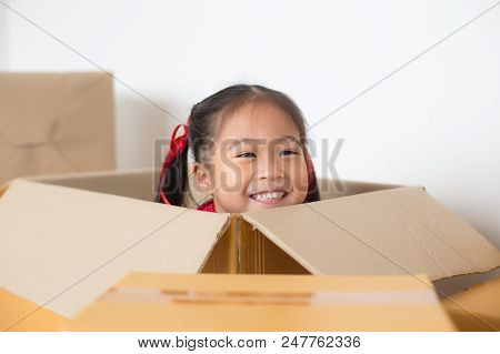 Asian Girl Playing In The Box At Home. Kid Sitting Inside Box With Attractive Smiling.