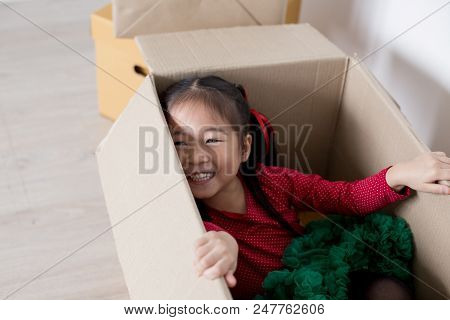 Asian Girl Playing In The Box At Home. Kid Sitting Inside Box With Attractive Smiling.