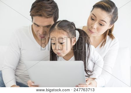 Attractive Little Girl Using Laptop With Mom And Dad Together. Girl Learning To Use Laptop. Happy Fa