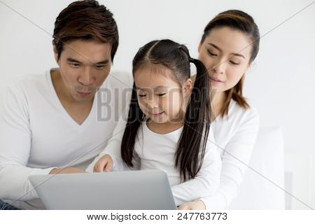 Attractive Little Girl Using Laptop With Mom And Dad Together. Girl Learning To Use Laptop. Happy Fa