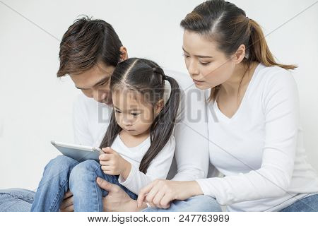 Little Girl Using Tablet With Dad And Mon Together At Home. People With Technology Concept.