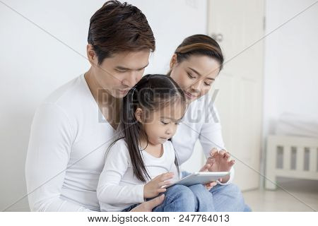 Little Girl Using Tablet With Dad And Mon Together At Home. People With Technology Concept.