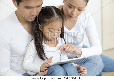 Little Girl Using Tablet With Dad And Mon Together At Home. People With Technology Concept.