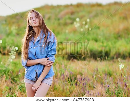 Happy Smiling Young Girl Wearing Blue Jeans Jacket And Shorts Is Standing In The Field