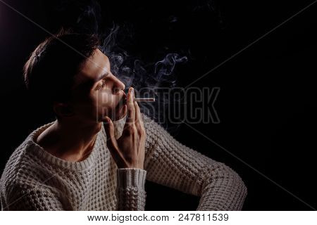 Thougtful Young Man, Wearing Warm Knitted White Sweater Smoking Sigarette, Thinking On Dark Backgrou