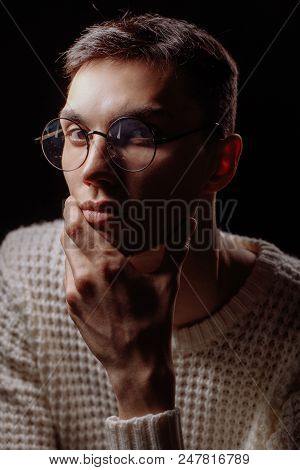 Studio Shot Of A Handsome Intelligent Student Guy In White Knitted Jersey, Looking At Camera With Th