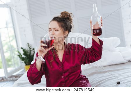 After Workday. Businesswoman Tasting Wine After Busy Workday While Sitting On Her Bed Wearing Pajama