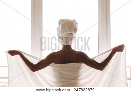 Back view of a young african woman wrapped in a towel standing in front of the wondow