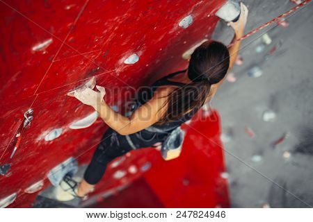 Unrecognizable Young Strong Woman Climbing On Rock Artificial Wall Top View. Female Climber Insured 
