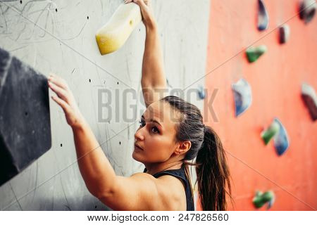 Beautiful Young Strong Woman Climbing On Rock Artificial Wall Top View. Female Climber Insured On Be