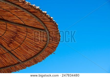 Straw Roof Of Sun Umbrella Against The Blue Sky. Vacation Topic.