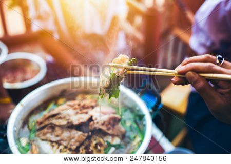 People cooking meat and grill. Food are vegeteble. People use chopsticks.
