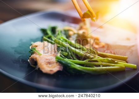 People cooking meat and grill. Food are vegeteble. People use chopsticks.