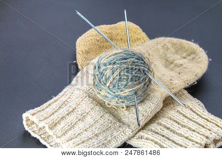 A Ball Of Wool With Knitting Needles And Socks On A Gray Table. Needlework