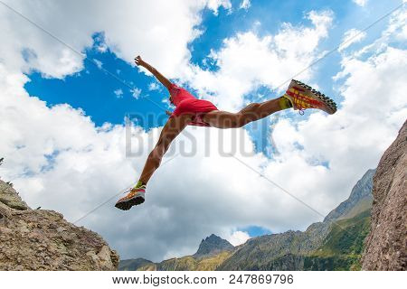 Girl Athlete With Great Physical Photographed From Under Jumps Between Two Stones