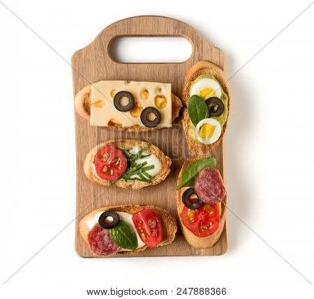 Open faced sandwich canape or crostini on a wooden serving board isolated on white background closeup. Top view.