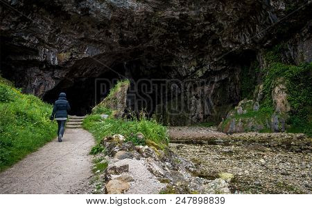 An Anonymous Tourist  Walking Into The Entrance Of Smoo Cave In Northern Scotland.