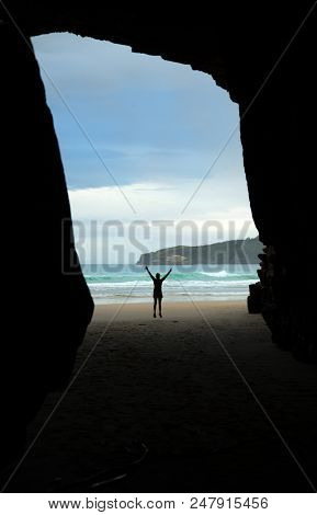 Woman jumping in the air at Cathedrale Cove in Catlins in New Zealand southern island