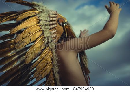 Prayer, Child playing at sunset dressed as an American Indian, wearing an Indian feather plume and breastplate. Field of wheat and nature