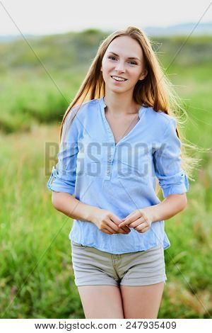 Happy Smiling Young Girl In Blue Shirt And Shorts In The Field