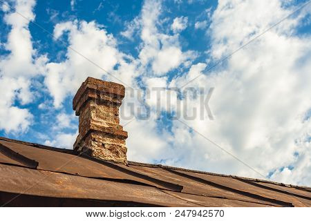 An Old Brick Pipe On The Roof Of A Residential Building With An Iron Roof Against A Background Of Cl