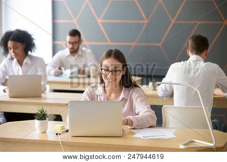 Smiling Young Employee Working At Laptop In Modern Coworking Office, Writing Message Or Checking Ema