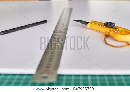 Cutter, Ruller And Pencil On A Green Mat And Wooden Table Background