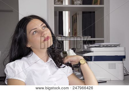 Portrait Of Good-looking Pensive Brunette Sitting Near Copy Machine At Work And Dreaming Looking Far
