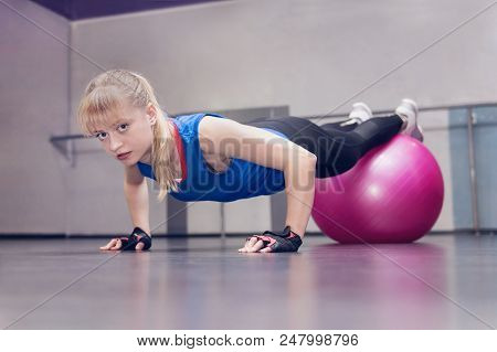 Attractive Blond Fitness Model Performing Push Ups With A Pink Fitball At The Gym.