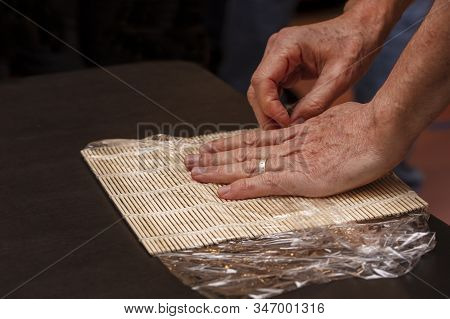 Chef Preparing Sushi Mat With Plastic Wrap To Make A Roll For A Cooking Class