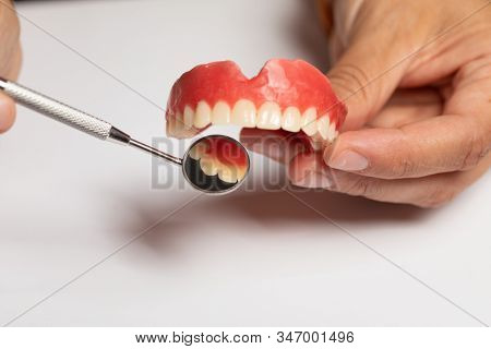 Denture prosthesis in doctor orthodentist dentist hand, checking with mirror